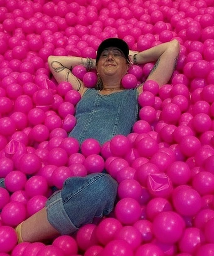 Person relaxing in a pool of bright pink balls.