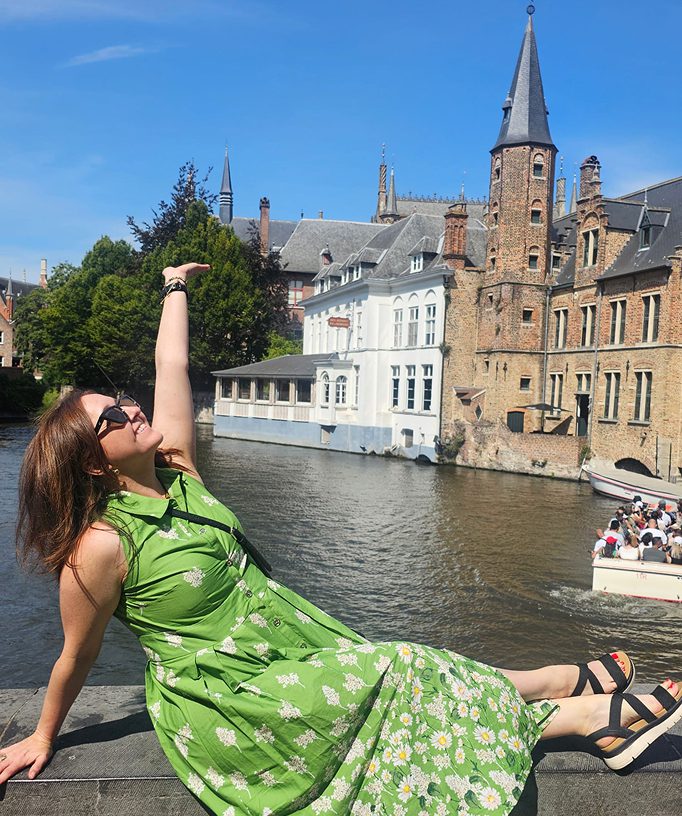 Woman in green dress enjoying a sunny day by a canal with historic buildings.