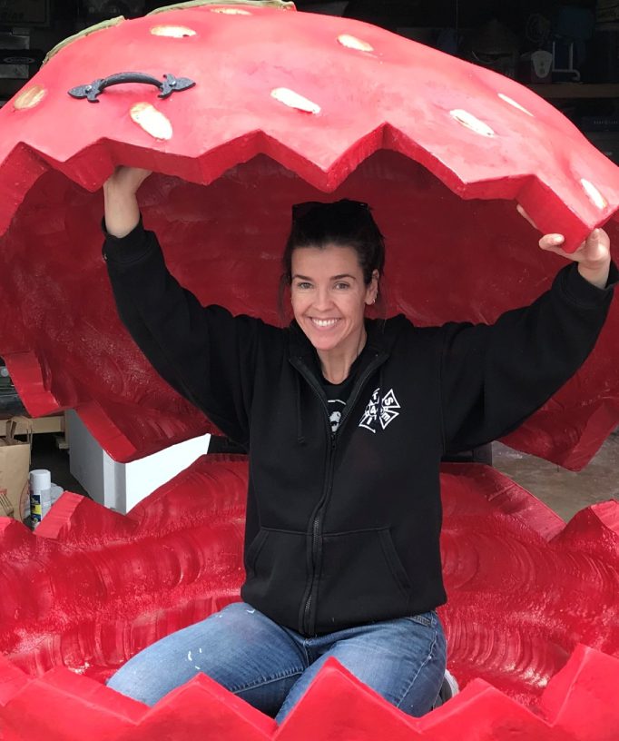 A woman smiling inside a large red sculpture that looks like a mouth.