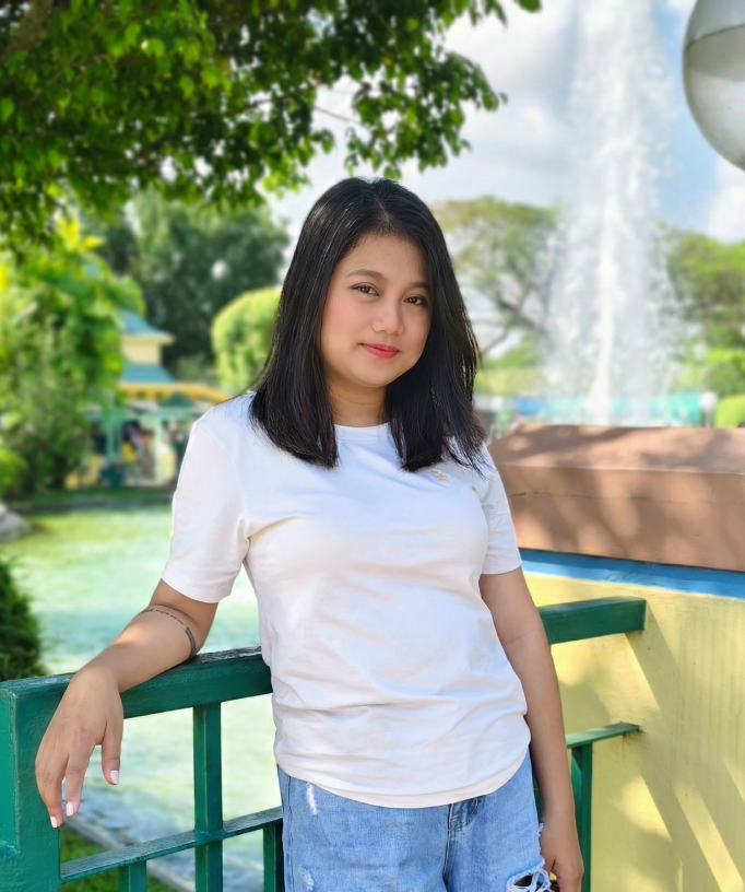 Young woman leaning on a railing by a fountain in a park.