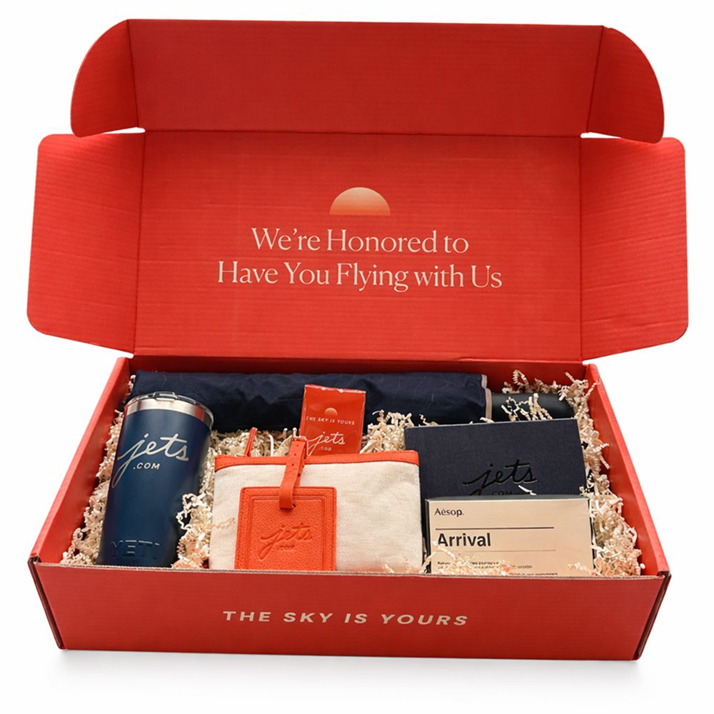 A red gift box with assorted items inside including candles and soaps.