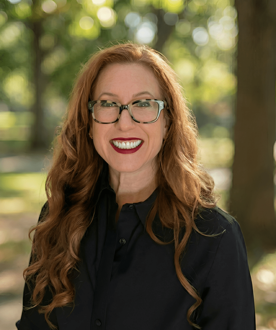 Smiling woman with long red hair and glasses outdoors.